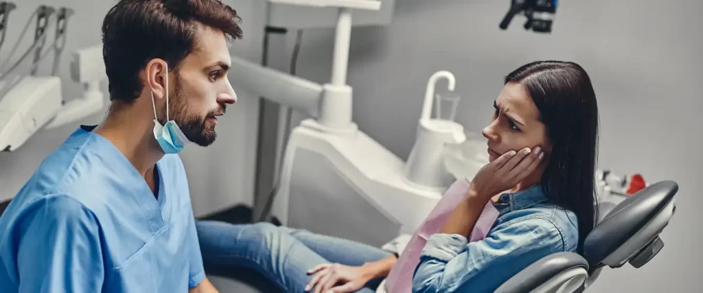 dentist talking to woman holding her jaw in pain